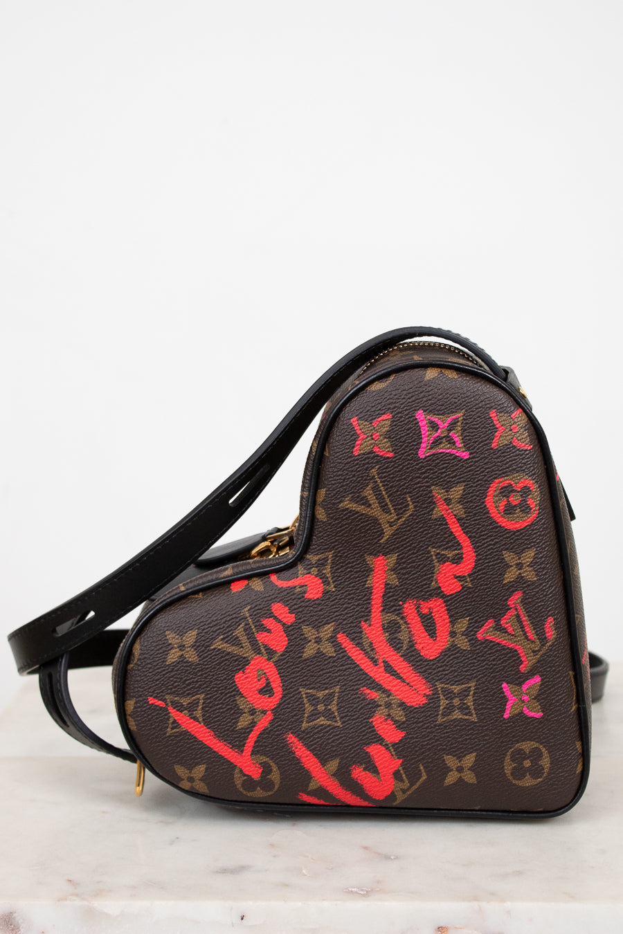 Heart-shaped handbag with Louis Vuitton monogram and graffiti-style text on a white background