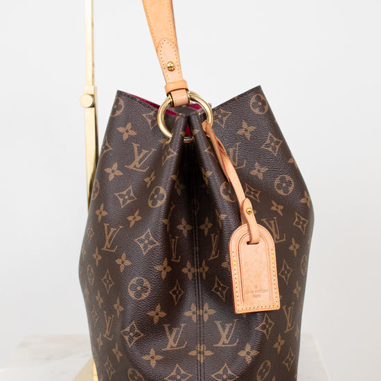 Louis Vuitton monogram handbag with tan leather handle and tag on a white background