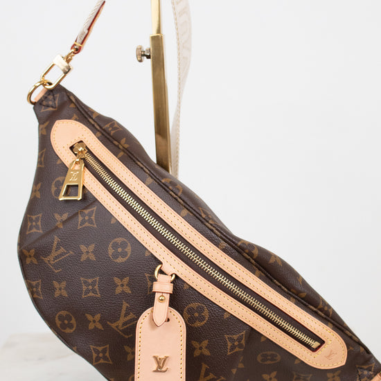 Louis Vuitton monogram coated canvas fanny pack with tan leather trim and gold-tone hardware, displayed on a gold stand against a white background.