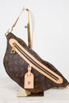 Louis Vuitton monogram coated canvas fanny pack with tan leather trim and gold-tone hardware, displayed on a gold stand against a white background.