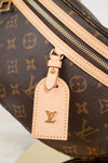 Close-up of a Louis Vuitton monogram bag in brown coated canvas with tan leather trim and a matching leather luggage tag featuring the embossed LV logo.