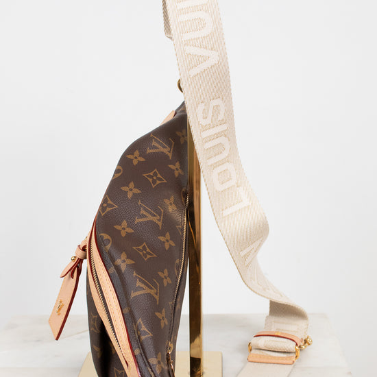 Louis Vuitton monogram shoulder bag in brown coated canvas with a beige canvas strap featuring white 'LOUIS VUITTON' text, displayed on a gold stand against a white background.