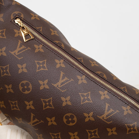 A close-up of a Louis Vuitton monogram coated canvas bag in dark brown with gold-tone zippers and hardware, resting on a light marble surface against a white background.