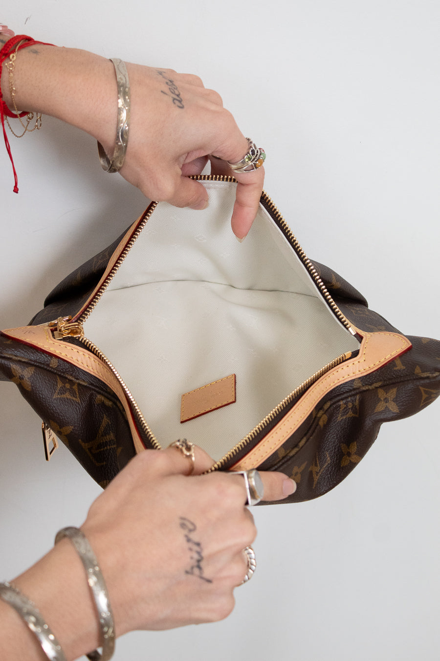 A Louis Vuitton monogram shoulder bag in brown coated canvas with tan leather trim, shown open with hands holding the zipper area. The interior is lined with light beige fabric, and a small tan leather brand patch is visible inside.