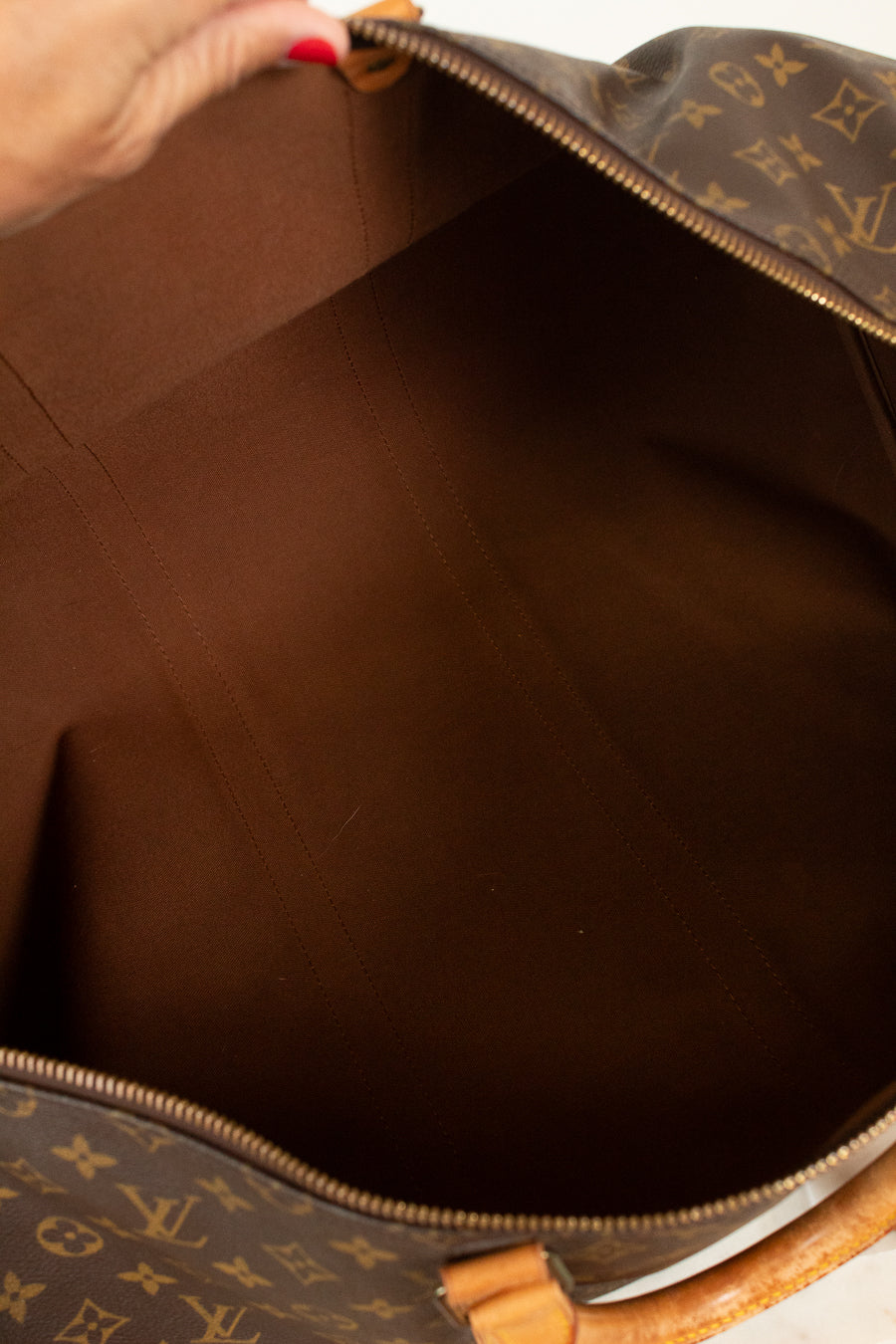 Hand wearing red nail polish holding open monogrammed bag showing brown textile interior
