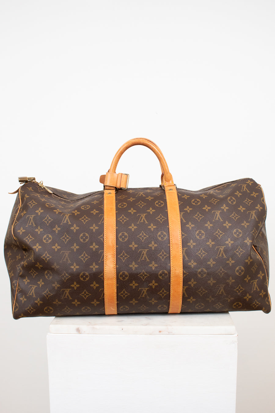 Large monogrammed duffel bag with leather trim details on white stand against light background