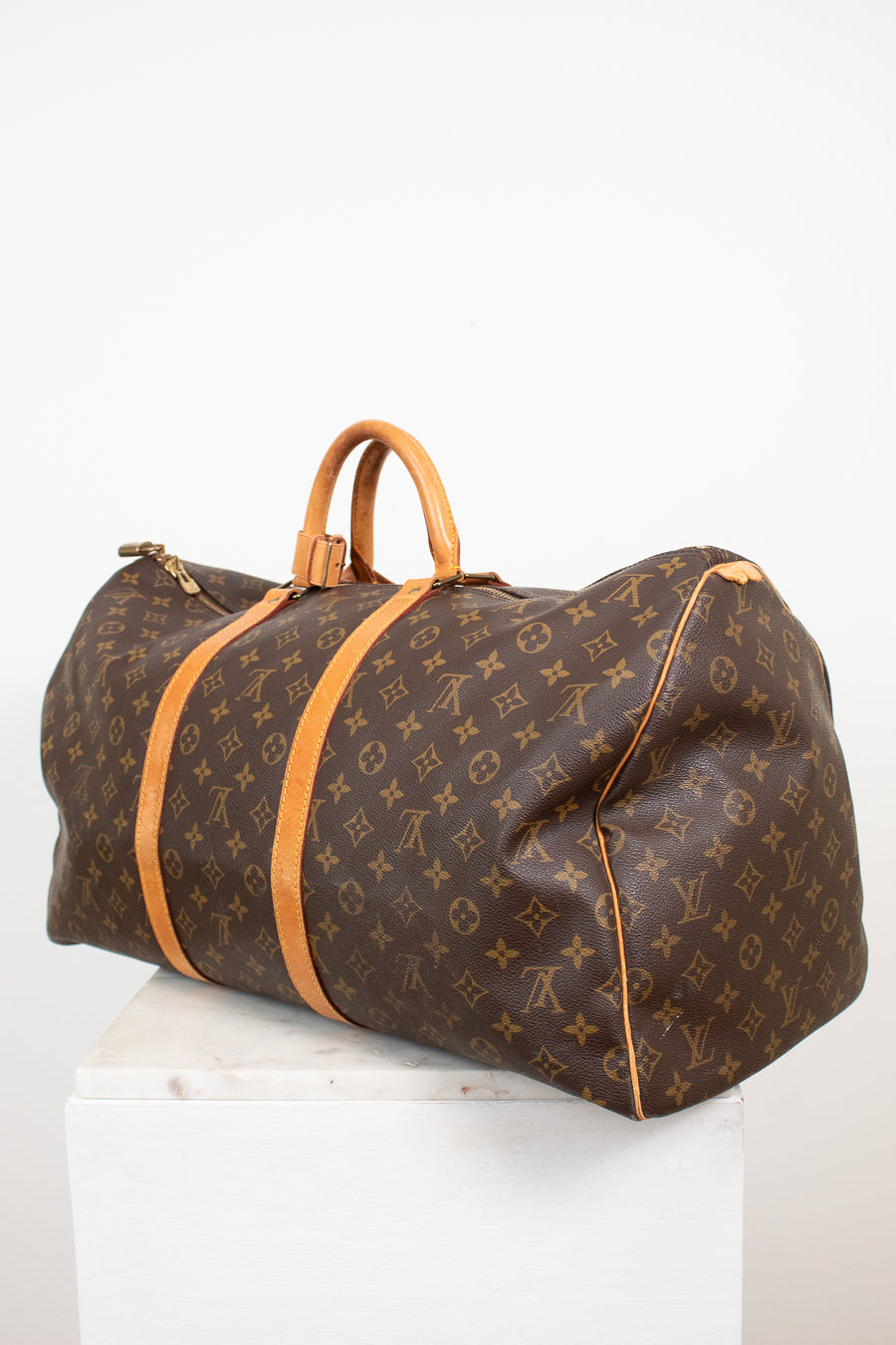 Large monogram coated canvas and tan leather duffel bag on white stand with light background