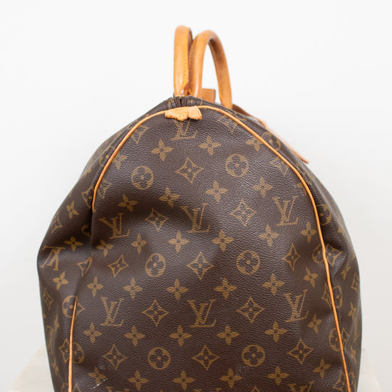 Side view of monogram duffel bag with visible rip of tan leather tab shown and tan leather handles showing against a light background