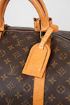 Close-up of tan leather tab with 'Louis Vuitton' branding visible attached to monogram coated canvas 