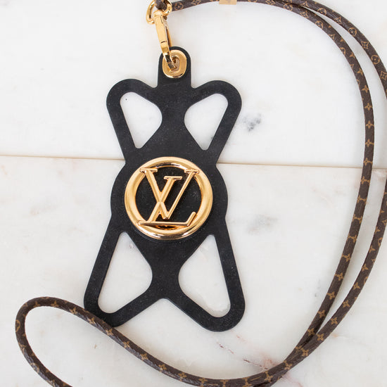A Louis Vuitton monogram leather strap with a black silhouette-shaped pendant featuring a gold-tone Louis Vuitton LV logo medallion, displayed on a light marble surface.