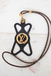 A Louis Vuitton monogram leather strap with a black silhouette-shaped pendant featuring a gold-tone Louis Vuitton LV logo medallion, displayed on a light marble surface.
