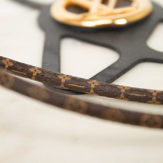 Close-up of a Louis Vuitton monogram canvas strap with gold-tone hardware and a black monogram-shaped plaque on a light marble surface.