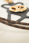 Close-up of a Louis Vuitton monogram canvas strap with gold-tone hardware and a black monogram-shaped plaque on a light marble surface.