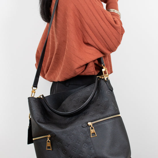 Person wearing a black handbag with gold zippers on a white background