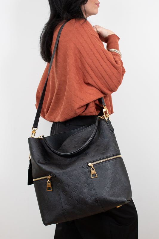 Person wearing a black handbag with gold zippers on a white background