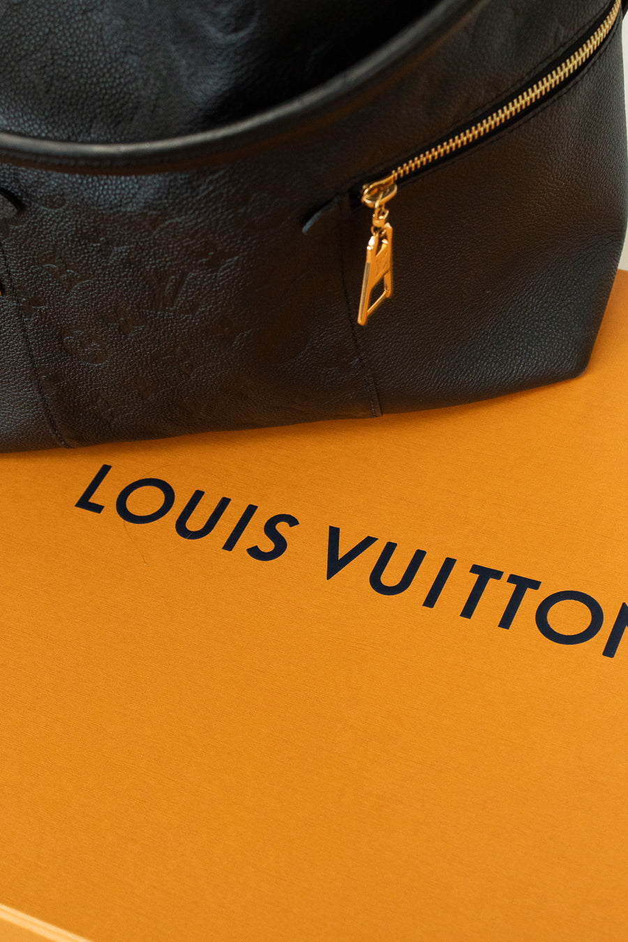 Black Louis Vuitton bag with gold zipper on a matching orange box background