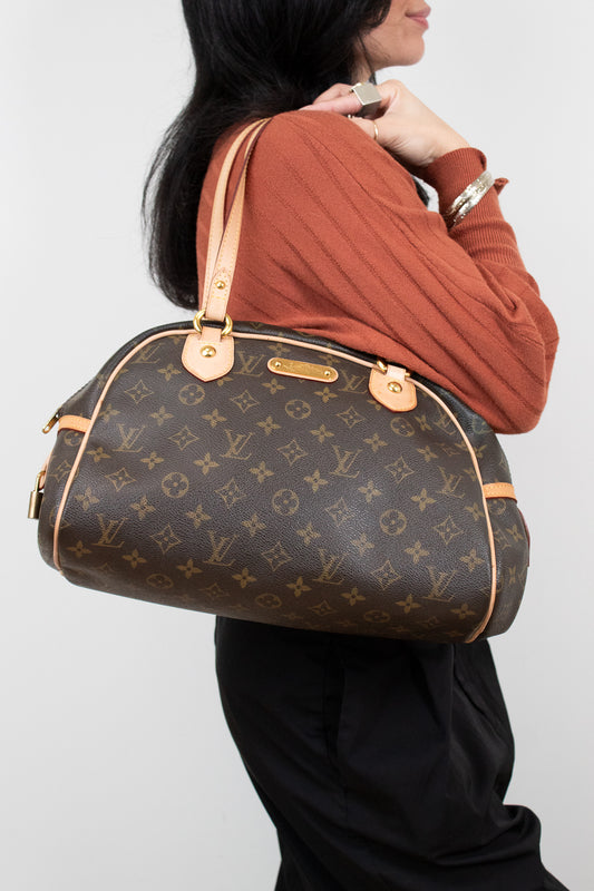 Person carrying a Louis Vuitton handbag against a plain background