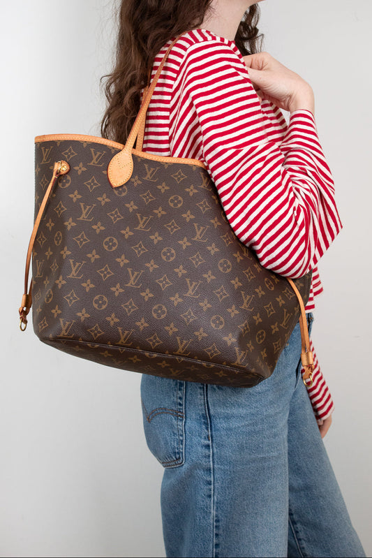 Person wearing a red and white striped shirt with a brown Louis Vuitton handbag on a plain background