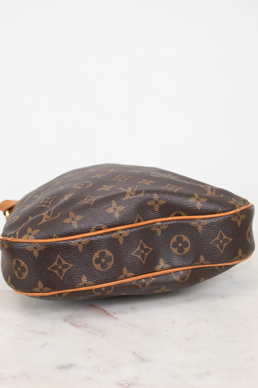 A Louis Vuitton monogram canvas shoulder bag in brown with tan leather trim, resting on a light marble surface against a white background.