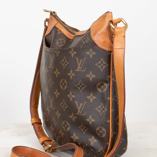 A Louis Vuitton monogram canvas shoulder bag with tan leather trim and strap, displayed on a light marble surface against a white background.