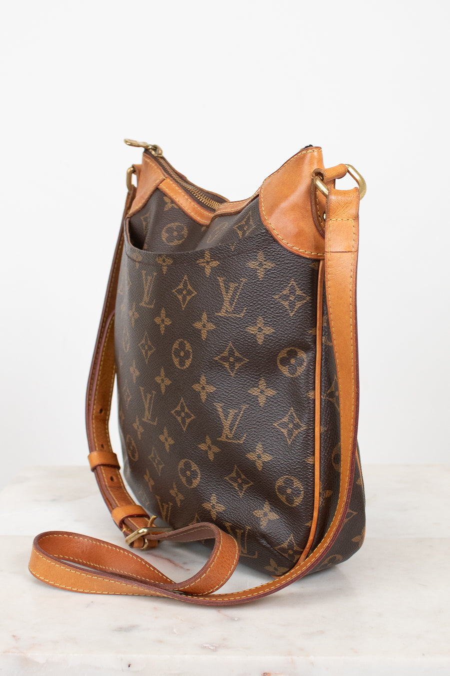 A Louis Vuitton monogram canvas shoulder bag with tan leather trim and strap, displayed on a light marble surface against a white background.