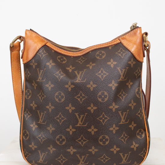 A Louis Vuitton monogram canvas shoulder bag with tan leather trim and a gold-tone zipper, displayed on a light marble surface against a white background.