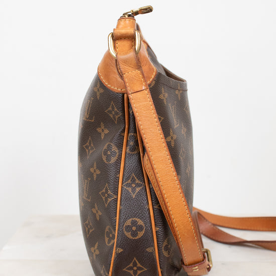 A Louis Vuitton monogram coated canvas shoulder bag shown from the side, featuring brown coated canvas with tan monogram motifs and light brown leather trim and strap, set against a plain white background.