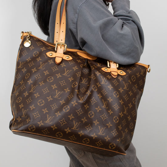 Person holding a large brown monogram handbag against a plain background