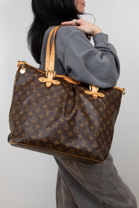 Person holding a large brown monogram handbag against a plain background
