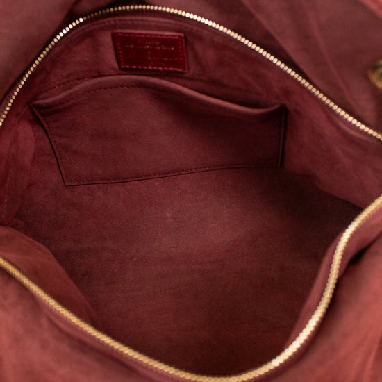 Close-up of the interior of a burgundy suede handbag, showing a zippered interior with a small pocket and a small leather brand patch inside.