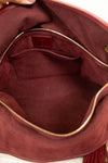 Close-up of the interior of a burgundy suede handbag, showing a zippered interior with a small pocket and a small leather brand patch inside.