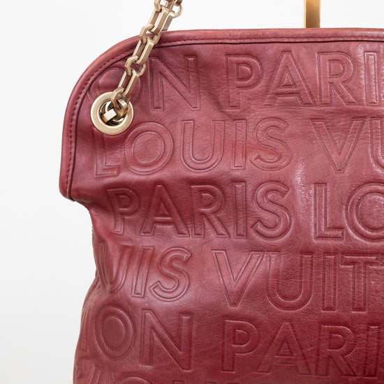 A close-up of a Louis Vuitton shoulder bag in burgundy leather with embossed 'LOUIS VUITTON PARIS' text, featuring a gold-tone chain strap and a gold metal ring attachment.