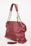 A Louis Vuitton shoulder bag in embossed burgundy leather, featuring gold-tone chain straps, a top handle, and a tassel detail, displayed on a white marble surface against a white background.