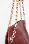 Close-up of a burgundy embossed leather handbag with a gold-tone chain strap against a white background.