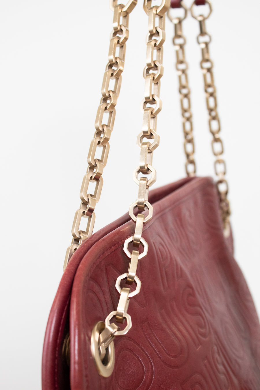 Close-up of a burgundy embossed leather handbag with a gold-tone chain strap against a white background.