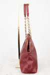A burgundy leather shoulder bag with embossed logo detailing and gold-tone chain straps, displayed on a gold stand against a white background.