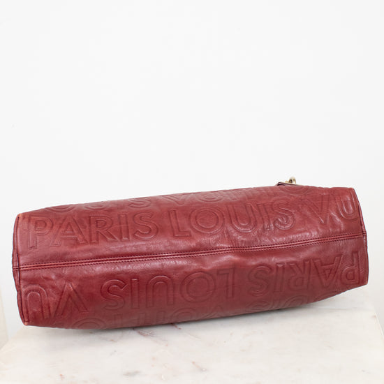A Louis Vuitton burgundy leather shoulder bag with an embossed monogram pattern, resting on a white marble surface against a white background.