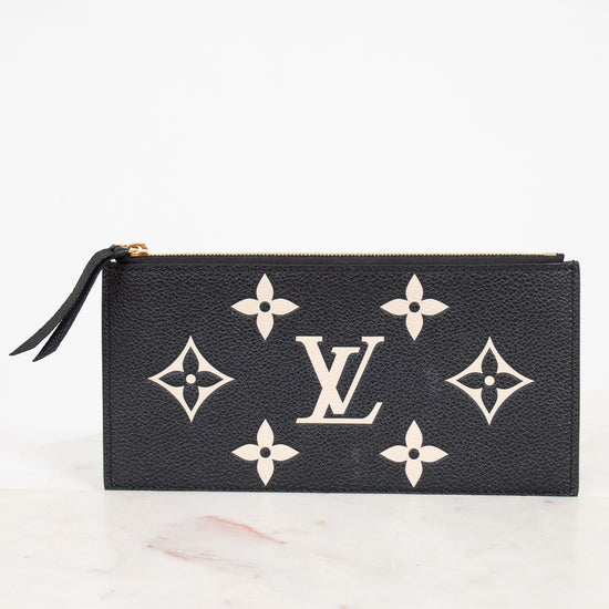 A black textured leather Louis Vuitton zip-around pouch featuring the classic beige monogram pattern and a central LV logo, resting on a light marble surface against a white background.