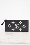 A black textured leather Louis Vuitton zip-around pouch featuring the classic beige monogram pattern and a central LV logo, resting on a light marble surface against a white background.