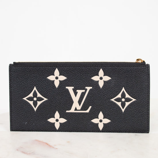 A black Louis Vuitton zip-around wallet or pouch made of textured leather, featuring the classic cream monogram pattern and LV logo on the front, set against a white background on a light marble surface.