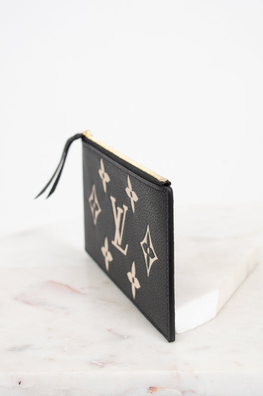 A black textured leather Louis Vuitton pouch featuring the classic beige monogram pattern, shown standing on a white marble surface against a white background.