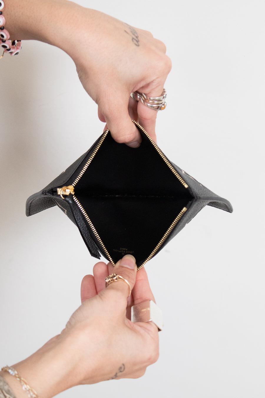 A close-up of a black leather zip-around card holder or small wallet being opened by two hands, showing a black interior and gold-tone zipper hardware against a plain light background.