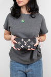 A woman wearing a gray t-shirt and blue jeans holds a black Louis Vuitton monogram pouch against a plain light gray background.