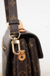 Close-up of a Louis Vuitton shoulder bag in brown monogram canvas with gold-tone hardware and a dark brown leather strap, shown against a plain light background.