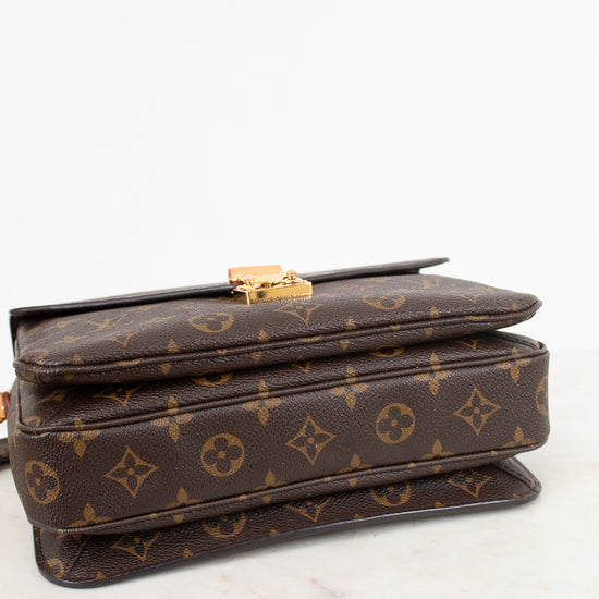 A Louis Vuitton monogram canvas shoulder bag in dark brown with gold-tone hardware, resting on a white marble surface against a white background.