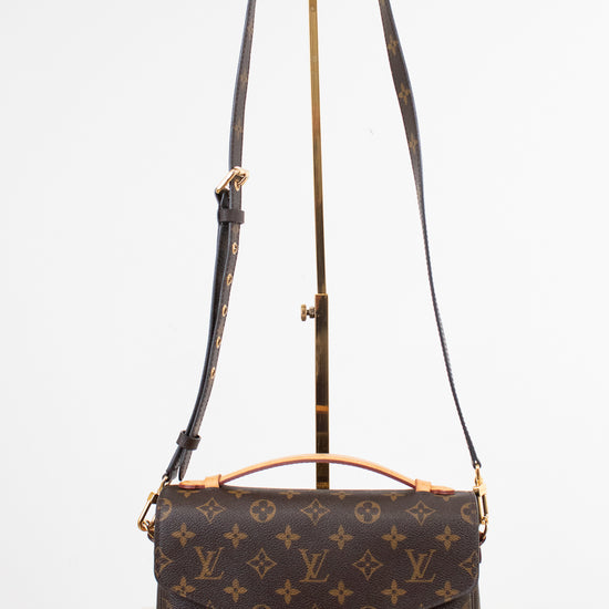 Louis Vuitton monogram canvas shoulder bag with a top handle and adjustable shoulder strap, displayed on a stand against a white background.