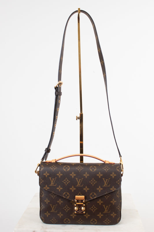 Louis Vuitton monogram canvas shoulder bag with a top handle and adjustable shoulder strap, displayed on a stand against a white background.