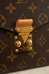 Close-up of a Louis Vuitton monogram handbag in brown coated canvas with gold-tone hardware and a tan leather strap tab, showing the Louis Vuitton Paris engraved clasp.