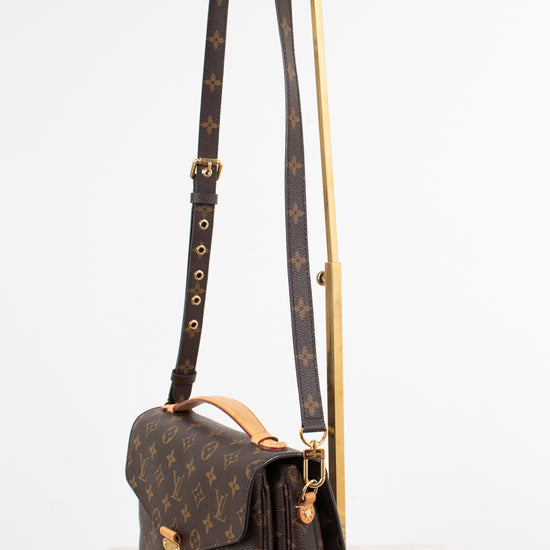 Louis Vuitton monogram shoulder bag in brown coated canvas with gold-tone hardware, displayed on a white surface with a gold stand against a white background.