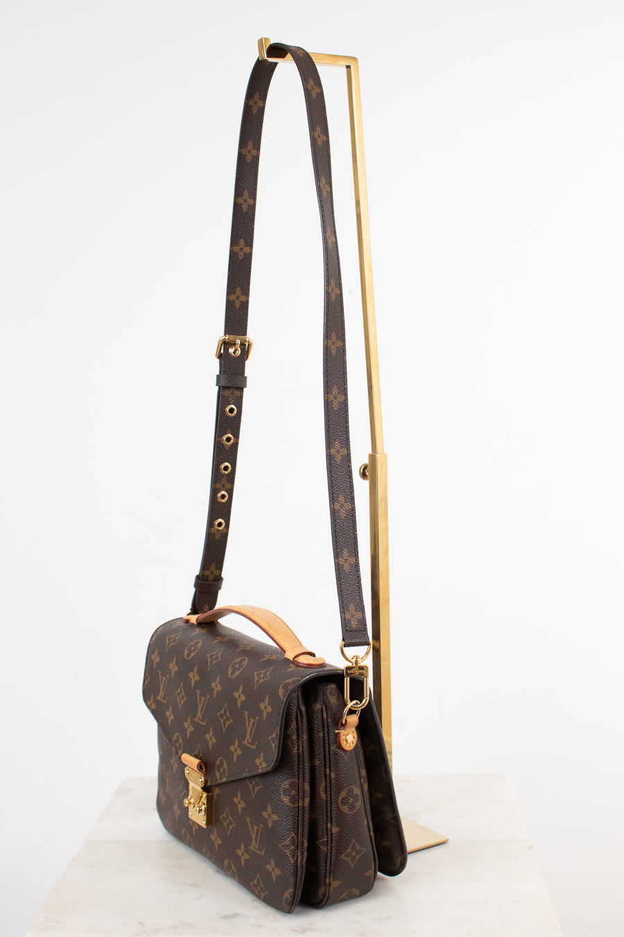Louis Vuitton monogram shoulder bag in brown coated canvas with gold-tone hardware, displayed on a white surface with a gold stand against a white background.